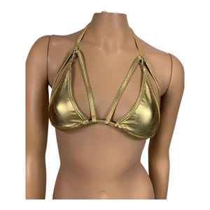 May include: A metallic gold bikini top with a halter neck and multiple straps. The top features a triangle cup design with silver-colored metal hardware. The fabric has a shiny, reflective finish.