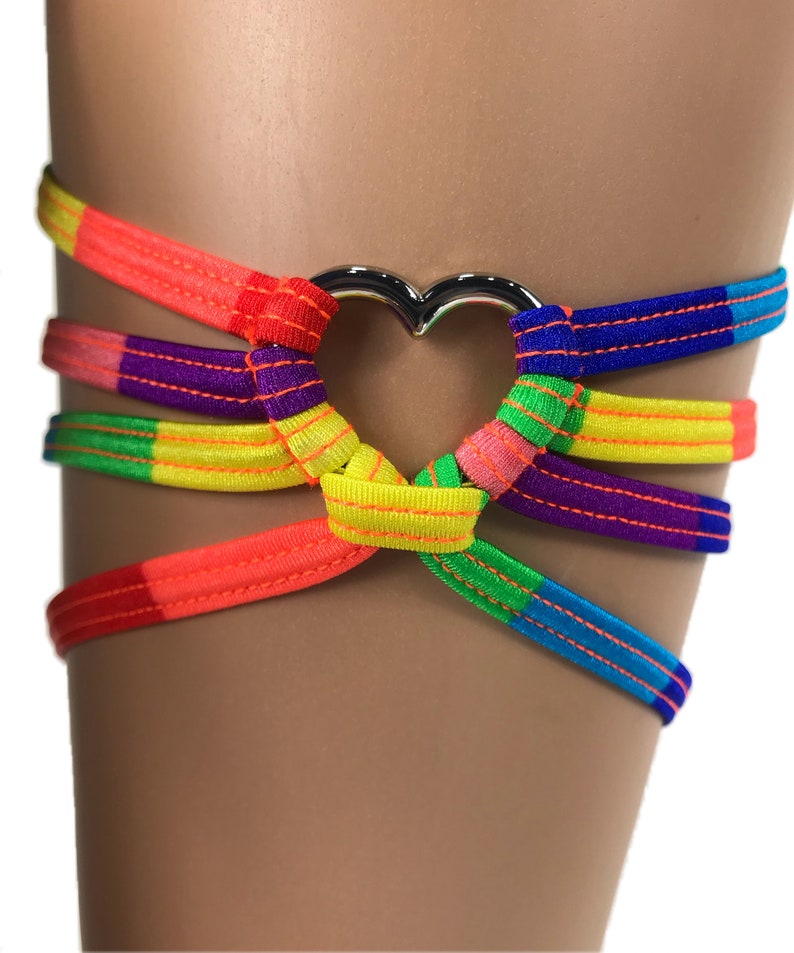 May include: Rainbow colored leg garter with a silver heart-shaped ring. The garter is made of elastic material and has a criss-cross design.