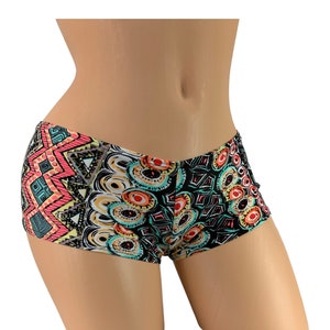 May include: Colorful patterned shorts with a low waist. The shorts feature a mix of geometric and abstract designs in shades of coral, teal, black, and yellow. The fabric appears to be a lightweight material, suitable for swimwear or casual wear.