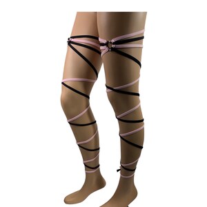 May include: Black and pink leg wraps with a metal ring on the upper thigh. The wraps are made of stretchy fabric and are designed to be worn around the legs.