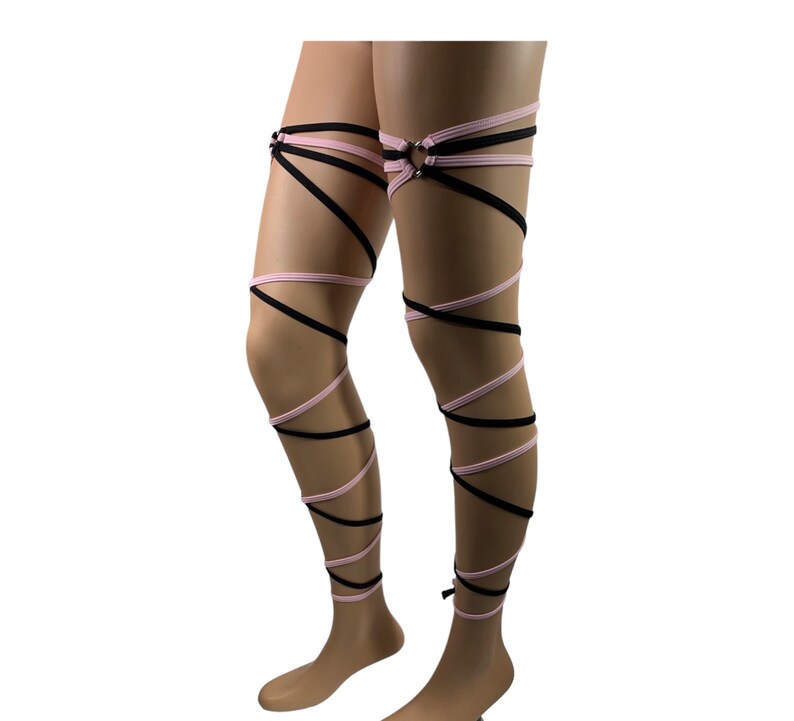 May include: Black and pink leg wraps with a metal ring on the upper thigh. The wraps are made of stretchy fabric and are designed to be worn around the legs.