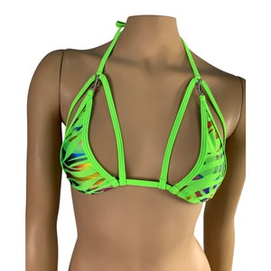 May include: Neon green bikini top with a halter neck and multiple straps. The fabric has a pattern of colorful, iridescent stripes. The top is designed with a unique cut-out style and silver-tone metal hardware.