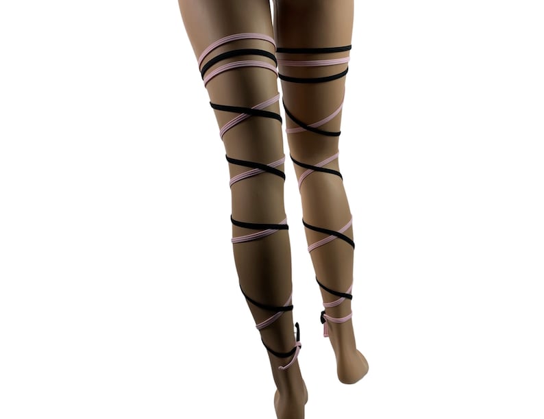 May include: A pair of black and pink leg wraps, worn on a model's legs. The wraps are tied in a criss-cross pattern, creating a unique and stylish look.