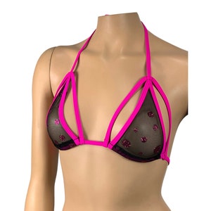 May include: A halter-style bikini top with a black mesh overlay and pink accents. The mesh is decorated with pink glitter dots. The top has a unique design with multiple straps and a halter neck.