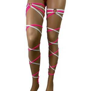 May include: A pair of leg wraps in a studio shot. The wraps are a combination of white and bright pink, with a crisscross design that wraps around the legs. The wraps are secured with metal rings at the top.