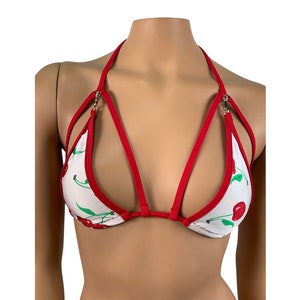 May include: A white and red cherry print bikini top with adjustable straps and a criss-cross design.