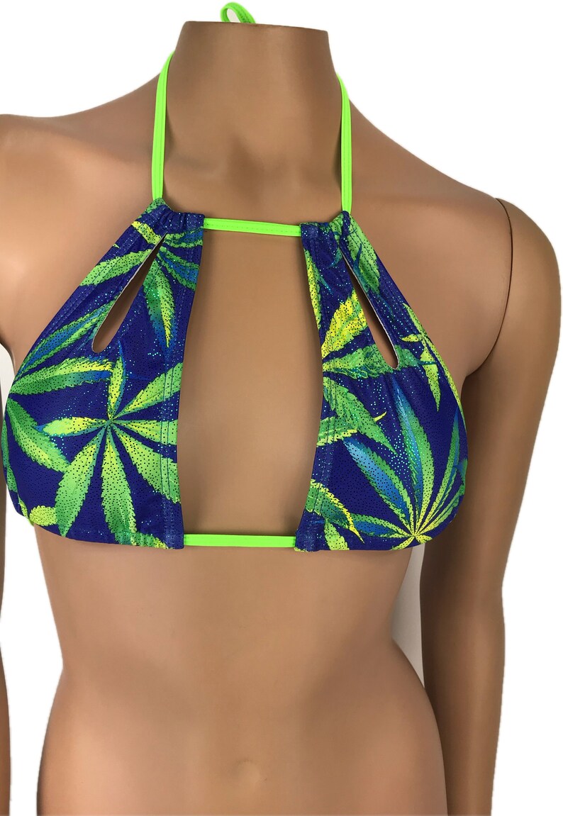 May include: A blue bikini top with a cannabis leaf pattern in green and yellow. The top has a halter neck and neon green trim. The design features a cutout in the center.