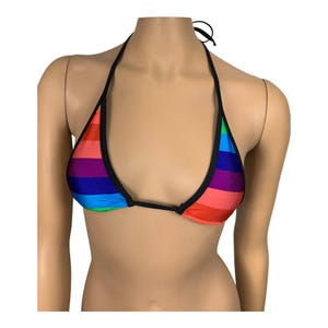 May include: A colorful rainbow striped bikini top with black trim. The top features a halter neck design and is made of a vibrant fabric with horizontal stripes in various colors, including red, orange, yellow, green, blue, and purple.