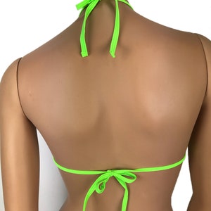 May include: Neon green bikini top with halter neck ties and back ties. The triangle top is made of a smooth, shiny fabric. The ties are knotted at the neck and back, creating a secure fit. The bright color makes it a standout swimwear piece.