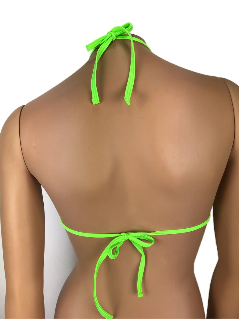 May include: Neon green bikini top with halter neck ties and back ties. The triangle top is made of a smooth, shiny fabric. The ties are knotted at the neck and back, creating a secure fit. The bright color makes it a standout swimwear piece.