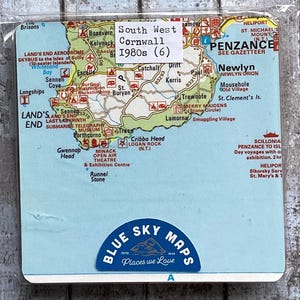 May include: A vintage map of South West Cornwall from the 1980s, featuring detailed geographical information. The map includes place names like Penzance, Land's End, and Newlyn. The map is labeled "Blue Sky Maps" and is in a plastic sleeve.