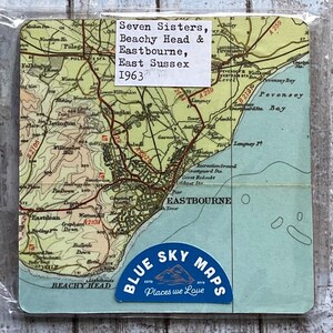 May include: A vintage map print of Eastbourne, East Sussex, featuring the Seven Sisters and Beachy Head, dated 1963. The map has a blue and beige color scheme, with a Blue Sky Maps sticker at the bottom. The print is encased in clear plastic.