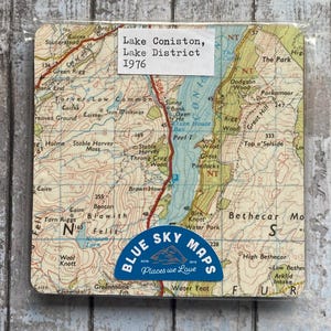 Puede incluir: Posavasos cuadrado con un mapa antiguo del lago Coniston, Lake District, de 1976. El posavasos tiene una pegatina azul y blanca que dice "Blue Sky Maps" y "Places we Love". El mapa muestra carreteras, elevaciones y nombres de lugares.