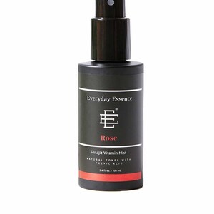 May include: A black bottle of Everyday Essence Rose Shilajit Vitamin Mist. The bottle has a black spray nozzle and a label with white text and a red stripe. The label reads "3.4 fl. oz. / 100 mL".