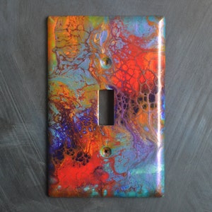 Puede incluir: Una tapa de interruptor de luz con un diseño abstracto con colores que se arremolinan en rojo, naranja, azul, verde y morado.