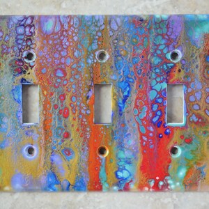 Puede incluir: Una cubierta de interruptor de luz colorida con un diseño abstracto en espiral en tonos de azul, rojo, amarillo y dorado.