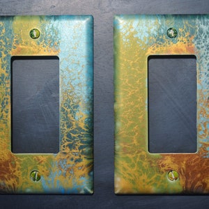 Puede incluir: Dos cubiertas de interruptor de luz decorativas con un diseño de pintura abstracta azul, verde y dorado.