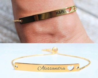 May include: Gold bracelet with a delicate chain and a bar charm engraved with "K&R" and a heart cut-out.