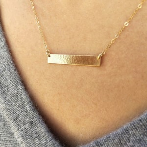 Puede incluir: Un collar de cadena de oro con un colgante de barra de oro martillado.
