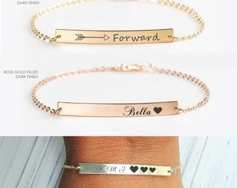 May include: Three gold bar bracelets with different engravings. The first bracelet has an arrow pointing to the right and the word "Forward" engraved on it. The second bracelet has the word "Bella" and a heart engraved on it. The third bracelet has the initials "KMJ" and three hearts engraved on it.