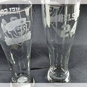 May include: Two clear glass beer pilsner glasses with etched designs. One glass features a football helmet and the word "Battalion". The other glass has the name "Nelson" and the number "24". The text "7T6DESIGNS" is at the bottom.