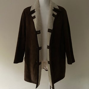 Puede incluir: Una chaqueta de ante marr&oacute;n con forro de piel sint&eacute;tica blanca. La chaqueta tiene cuello y cierre de botones.