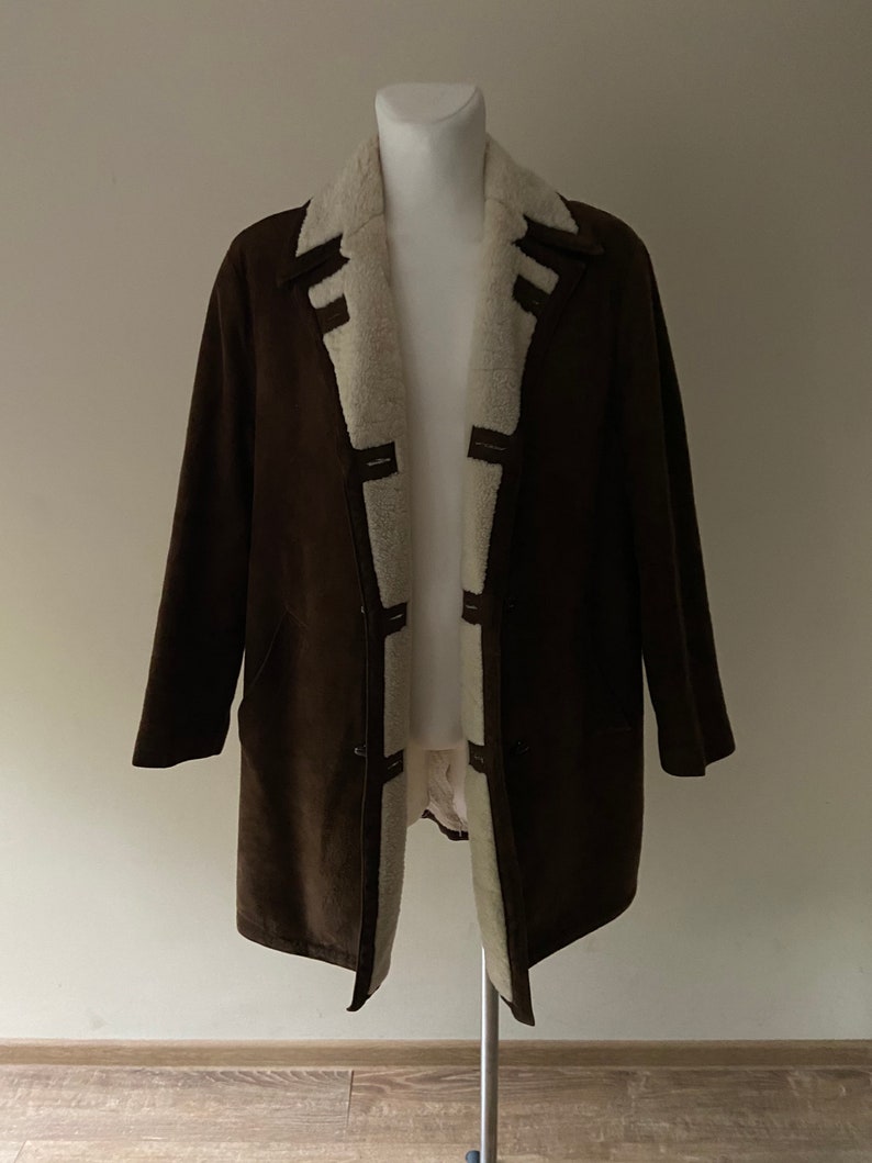 Puede incluir: Una chaqueta de ante marr&oacute;n con forro de piel sint&eacute;tica blanca. La chaqueta tiene cuello y cierre de botones.