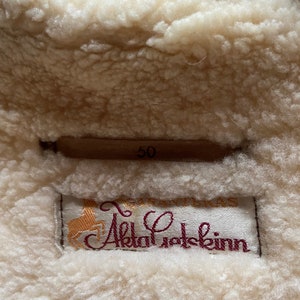 Puede incluir: Primer plano de una etiqueta de abrigo de piel de oveja blanca con el texto "GIRAFFE Alpakafotskinn" y el n&uacute;mero "50" impreso en ella.