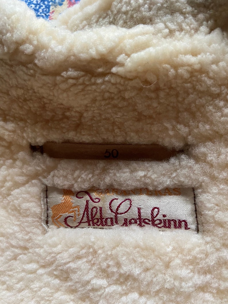 Puede incluir: Primer plano de una etiqueta de abrigo de piel de oveja blanca con el texto "GIRAFFE Alpakafotskinn" y el n&uacute;mero "50" impreso en ella.