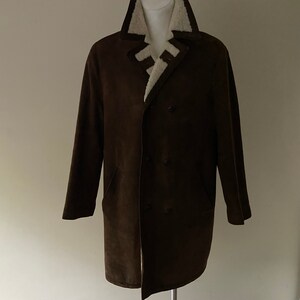 Puede incluir: Un abrigo de ante marr&oacute;n con cuello de piel sint&eacute;tica blanca y cierre de doble botonadura.