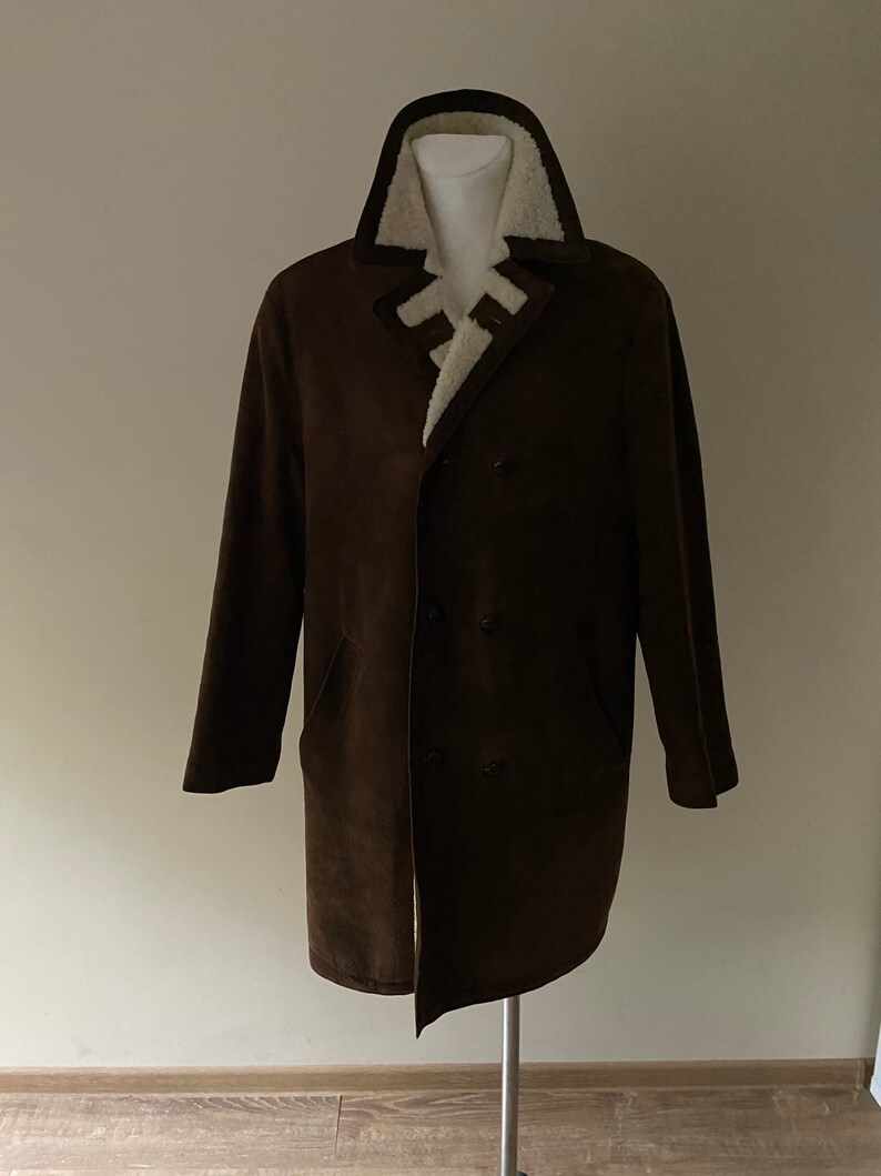 Puede incluir: Un abrigo de ante marr&oacute;n con cuello de piel sint&eacute;tica blanca y cierre de doble botonadura.