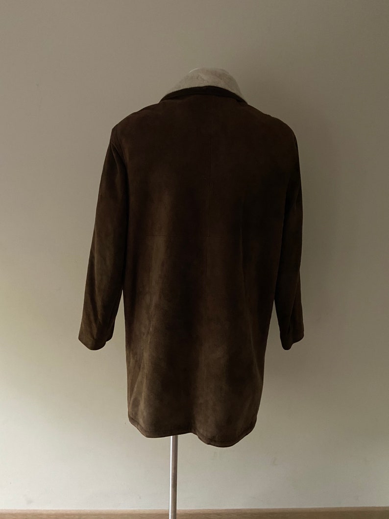 Puede incluir: Una chaqueta de ante marr&oacute;n con cuello de piel blanca.