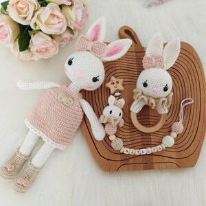 May include: Two crocheted bunny toys with pink accents, one wearing a pink dress and the other with a wooden ring, on a wooden tray with the name "Natalia" spelled out in wooden letters.