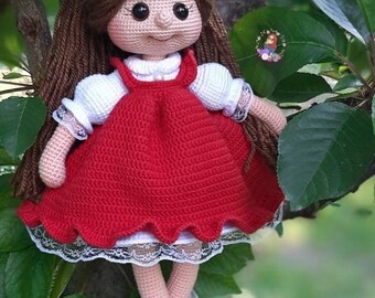 May include: A crocheted doll with brown hair, a red dress, and white socks and shoes. The doll is sitting on a tree branch.
