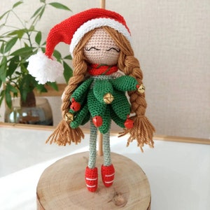May include: A crocheted Christmas tree doll with a red hat, brown hair, and green dress. The doll is wearing red shoes and has a white trim on the hat.