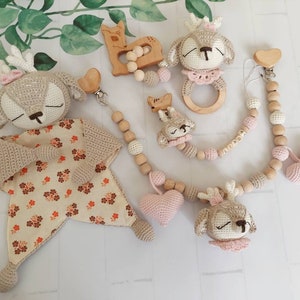 Op de afbeelding: Een set gehaakte herten speelgoed voor baby's, inclusief een rammelaar, een bijtring en een zacht knuffeldier. De speelgoed is in beige, bruin en roze tinten.