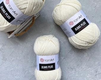 Pode incluir: Três novelos de fio branco com a etiqueta "YarnArt Jeans Plus".