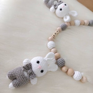 May include: A gray and white crocheted bunny toy with a bow tie attached to a wooden bead garland with the name "EFE" spelled out on the beads.
