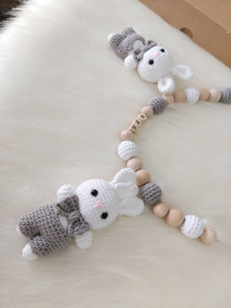 May include: A gray and white crocheted bunny toy with a bow tie attached to a wooden bead garland with the name "EFE" spelled out on the beads.