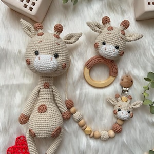 May include: A crocheted giraffe toy with a wooden ring and a beaded chain with a smaller crocheted giraffe head. The giraffe toy is beige with brown spots and the chain has wooden beads and a brown wooden bead with a geometric shape.