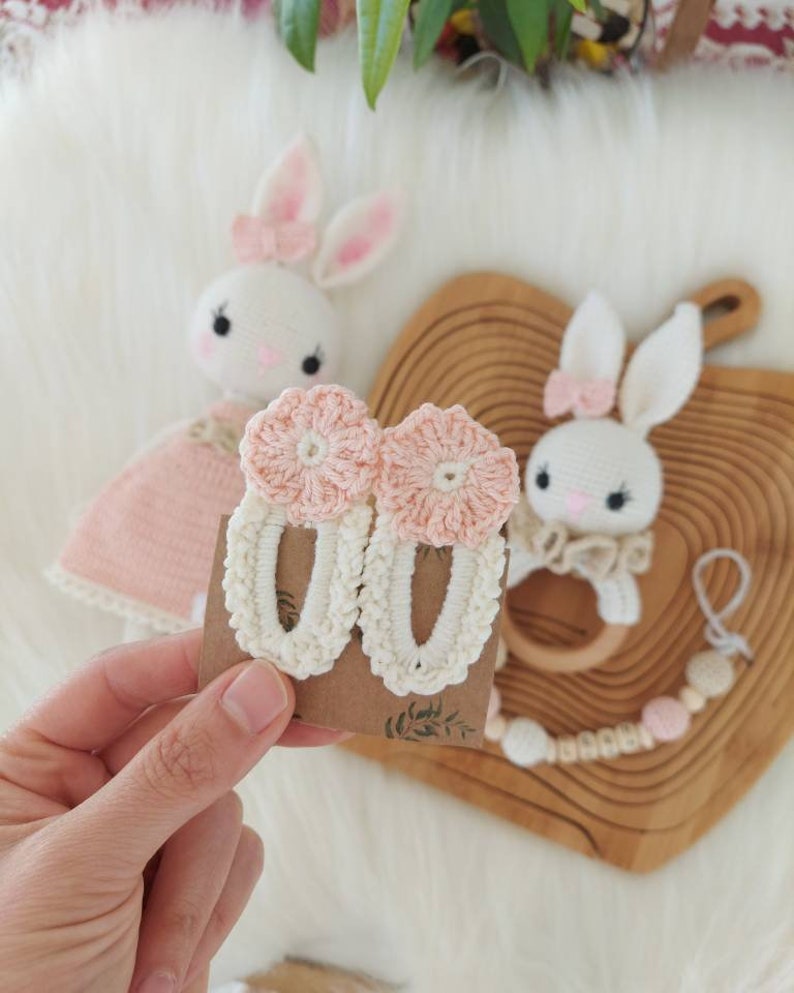 May include: A pair of crocheted hair clips with pink flower accents. The clips are white with a delicate crocheted design.