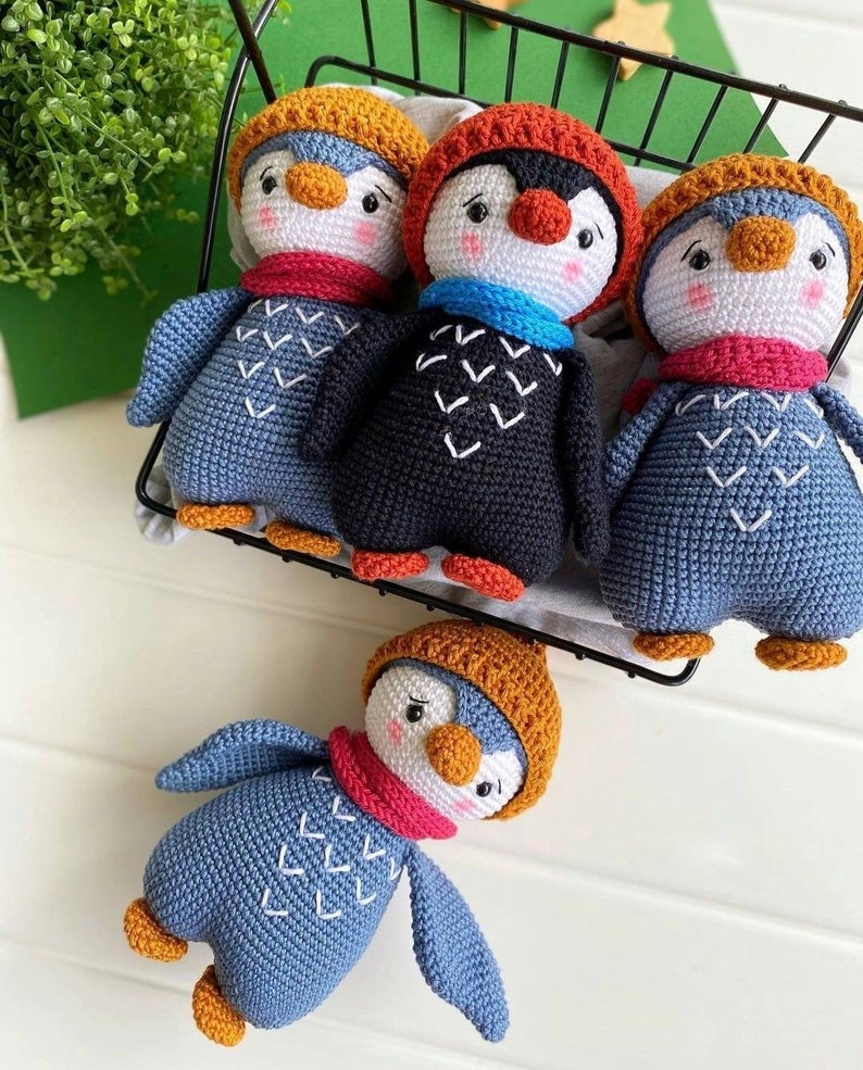 May include: Four crocheted penguin toys with different colored hats and scarves. The penguins are sitting in a black wire basket.