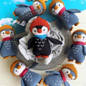 May include: A group of crocheted penguin toys in various colors, including blue, black, and orange. The penguins are wearing hats and scarves and have embroidered details. The toys are arranged in a circle on a black wire mesh surface.