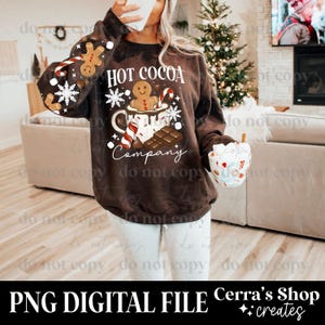 May include: A brown sweatshirt with a "Hot Cocoa Company" design featuring a gingerbread man, snowflakes, candy canes, and chocolate. The sleeves have gingerbread men and snowflakes. The image also includes a cup of cocoa.