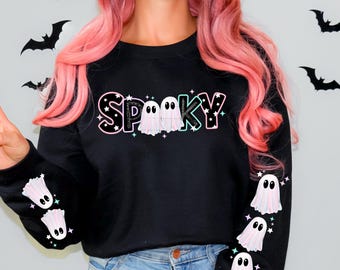 May include: Black sweatshirt with the word "Spooky" in a bubble font with two ghost figures. The sleeves feature ghost graphics with stars. The design has pink, green, and white accents, perfect for Halloween.