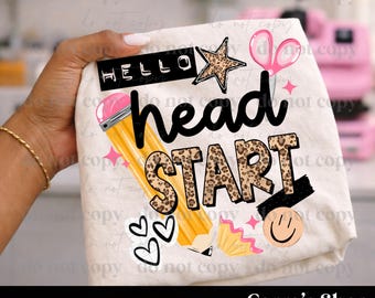 May include: A white fabric item featuring a graphic design with the text HELLO head START. The design includes a yellow pencil, a leopard print star, pink scissors, a smiley face, three black heart outlines, and a pink pencil shaving.