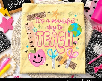 May include: A pale yellow t-shirt featuring the text It's a beautiful day to TEACH in pink and orange. The design includes a ruler, a pink smiling apple, blue scissors, a yellow pencil, a pink pair of scissors, and a globe graphic.