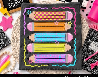 May include: A dark gray t-shirt featuring a graphic print of five horizontal pencils in yellow, orange, light blue, lime green, and purple. The pencils have pink erasers and are surrounded by a wavy neon border with small star accents.