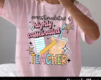 May include: A light pink t-shirt featuring a graphic with the text "overstimulated & highly caffeinated TEACHER". The design includes a notebook, a pencil, a lidded cup with a straw, and star shapes with leopard print and black outlines.