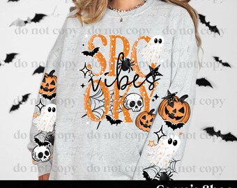 May include: A light gray crewneck sweatshirt featuring the orange text SPOOKY and the black script text vibes. The design includes illustrations of white ghosts, orange jack-o'-lanterns, black skulls, spiders, spiderwebs, stars, and bats.